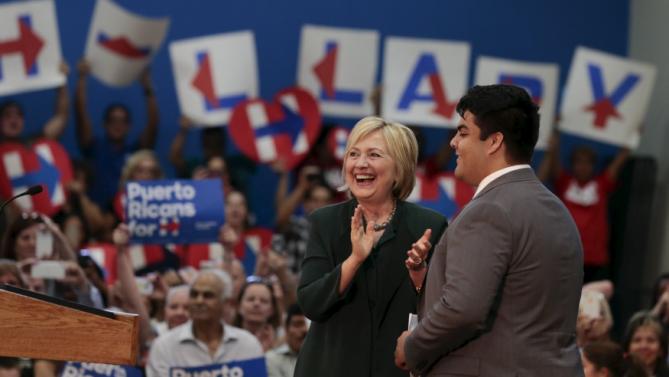 U.S. Democratic presidential candidate Hillary Clinton (C) walks on stage with John Quiroz, a former local college student before speaking at an election campaign event in Orlando, Florida December 2, 2015. REUTERS/Scott Audette