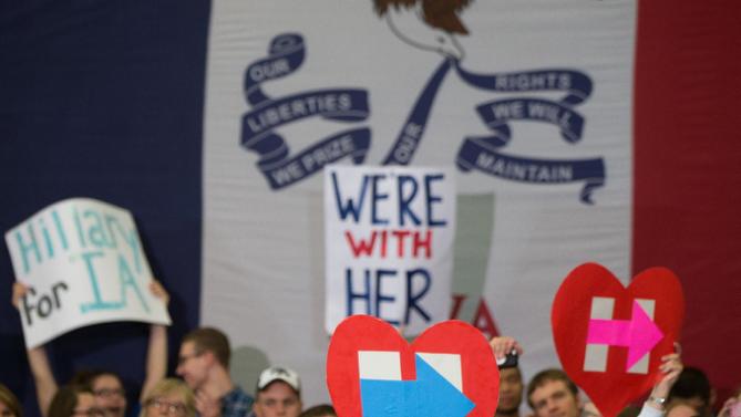 Members of the audience hold signs in front of a large Iowa state flag as Democratic presidential candidate Hillary Clinton speaks at a rally at Washington High School in Cedar Rapids, Iowa, Saturday, Jan. 30, 2016. (AP Photo/Andrew Harnik)
