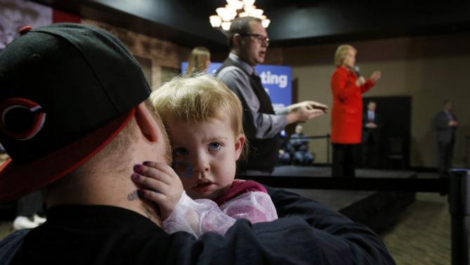 A young child hugs her father as U.S. Democratic presidential candidate Hillary Clinton (R) addresses a campaign event in Carroll, Iowa January 30, 2016. REUTERS/Jim Bourg